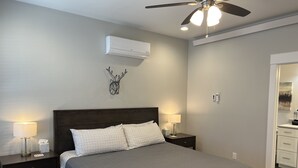A bedroom with a bed, two bedside tables, a wall-mounted air conditioner, a ceiling fan, and a decorative deer head on the wall. - Beautiful New Luxury Condo in Downtown Salida! #0676 (Salida)