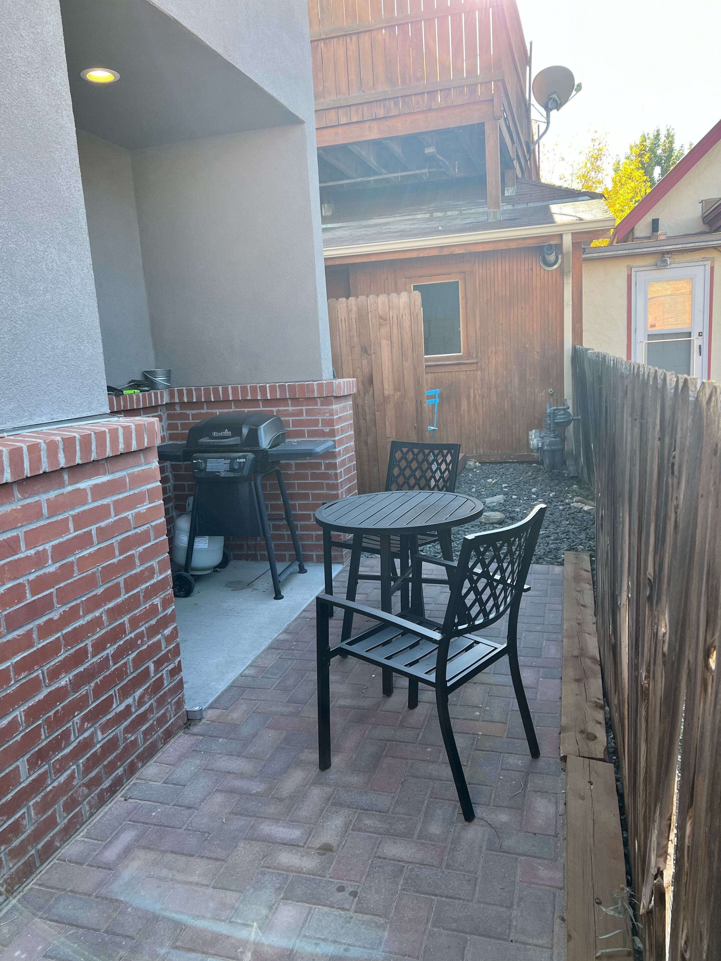 A patio with a brick wall, a grill, and a round table with chairs.