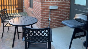 An outdoor patio with a brick wall, a table, two chairs, and a grill. - Beautiful New Luxury Condo in Downtown Salida! #0676 (Salida)