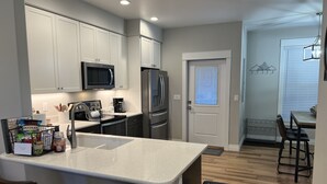 A modern kitchen with white cabinets, stainless steel appliances, a central island with bar stools, and a dining area with a wooden table and chairs. - Beautiful New Luxury Condo in Downtown Salida! #0676 (Salida)