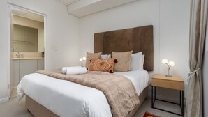 Une chambre avec un grand lit, une table de chevet avec une lampe, un miroir et une vue sur la salle de bain.