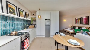 A modern kitchen with a stove, oven, and refrigerator, a dining table with plates, and a sofa in the living area. - Refurbished Studio Apart in the Heart of Cape Town

 (Cape Town)