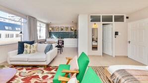 A modern living room with a sofa, green armchair, and a bed. There is a kitchen area in the background with a view of the city. - Refurbished Studio Apart in the Heart of Cape Town

 (Cape Town)