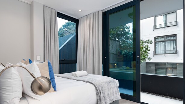 Un dormitorio moderno con una cama grande, vistas al balcón exterior y una puerta corrediza de vidrio.