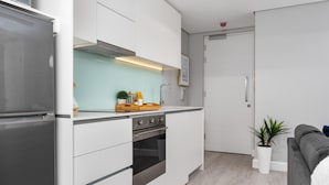 Una cocina moderna con armarios blancos, un refrigerador de acero inoxidable y un horno. Hay una pequeña encimera con una planta y un marco de fotos.