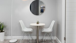 Una habitación moderna con una mesa redonda, dos sillas blancas, una lámpara de pie y una planta en maceta.