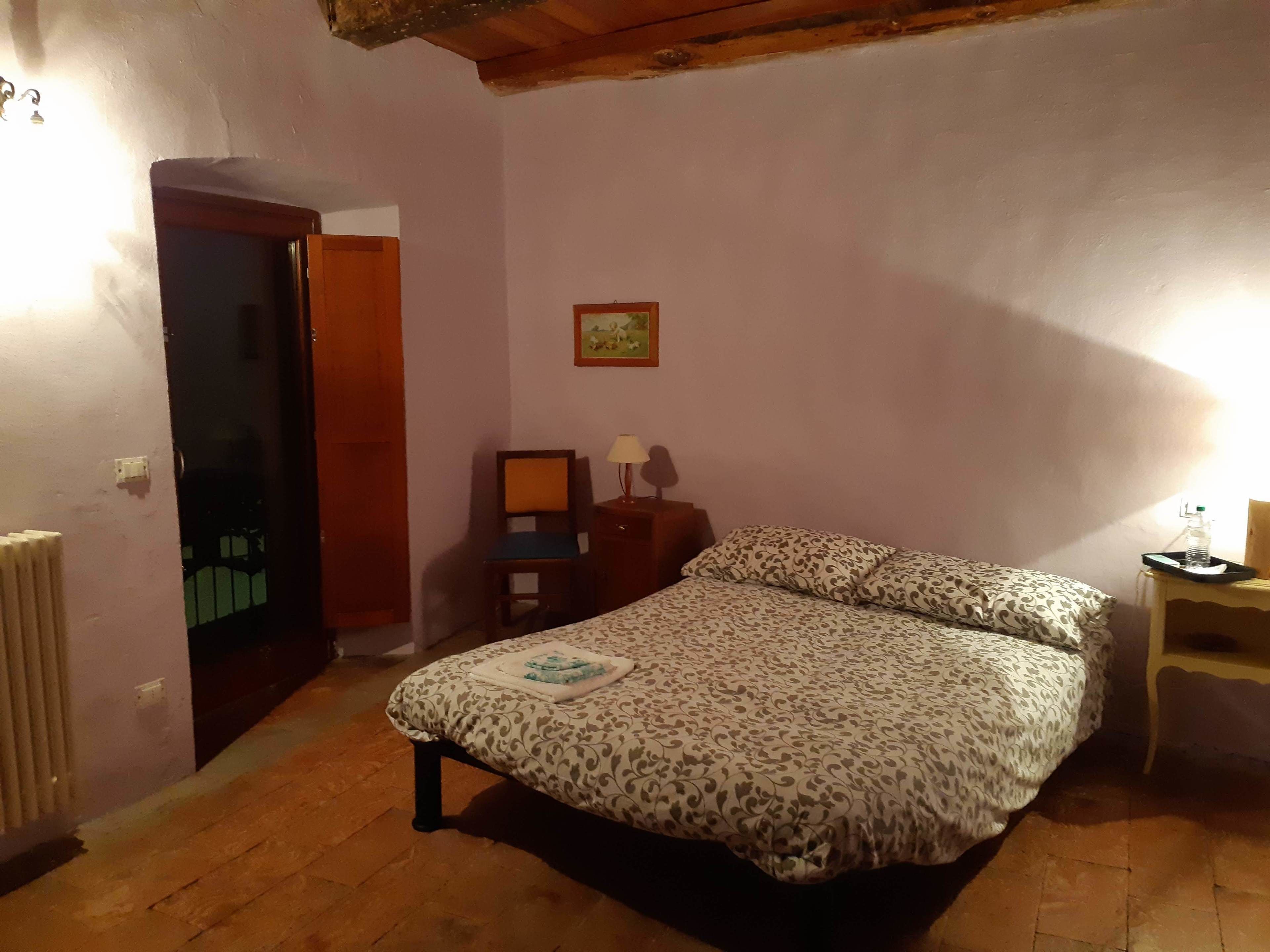 Une chambre à coucher avec un lit, une chaise, une petite table avec une lampe et un radiateur.