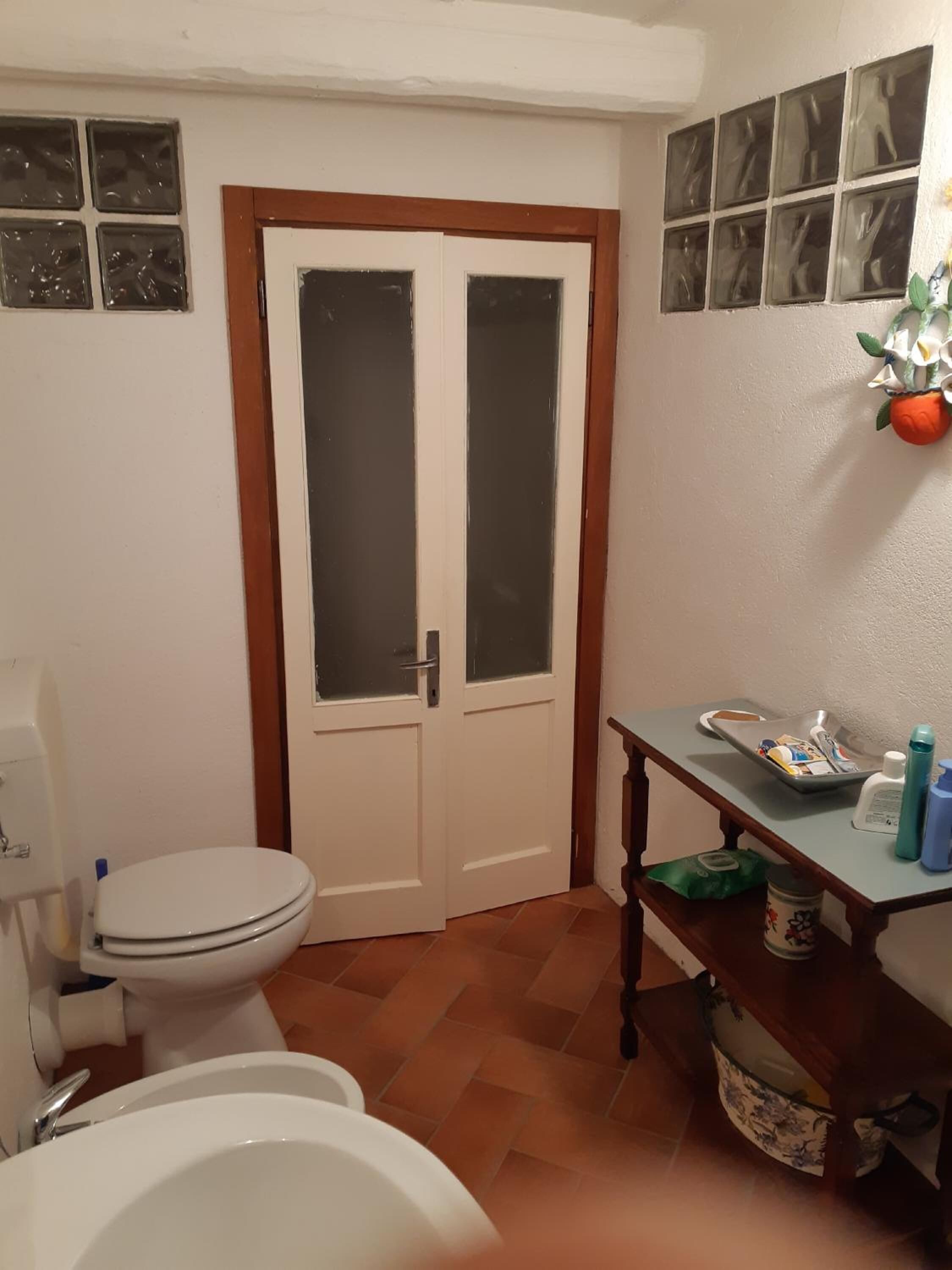 A bathroom with a toilet, sink, and a small table with toiletries.