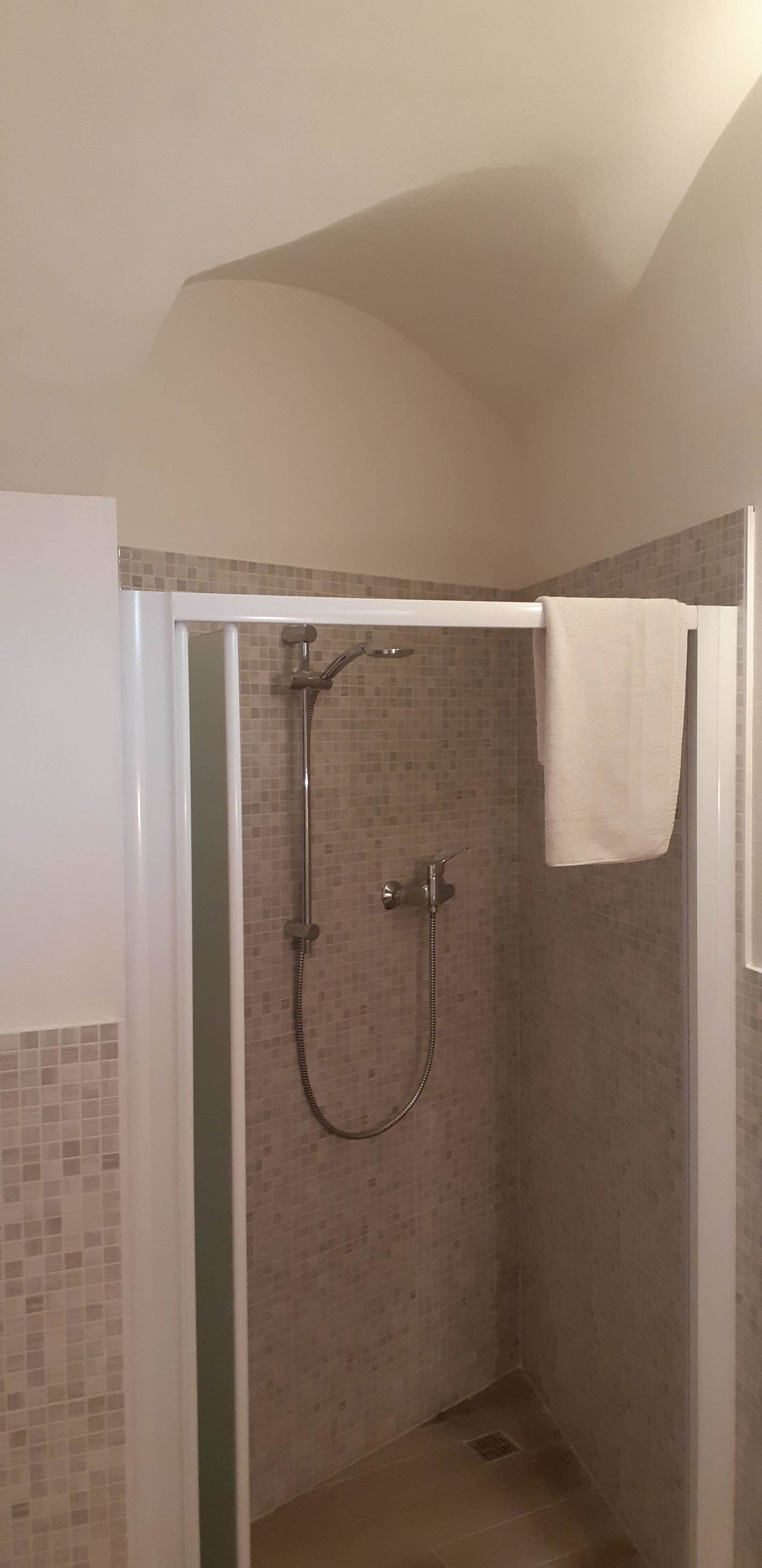 Eine Dusche mit Glastür, gefliesten Wänden und einem Handtuch, das an der Tür hängt.