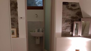 Un dormitorio con cama, mesita de noche, espejo y baño visible a través de una puerta abierta.