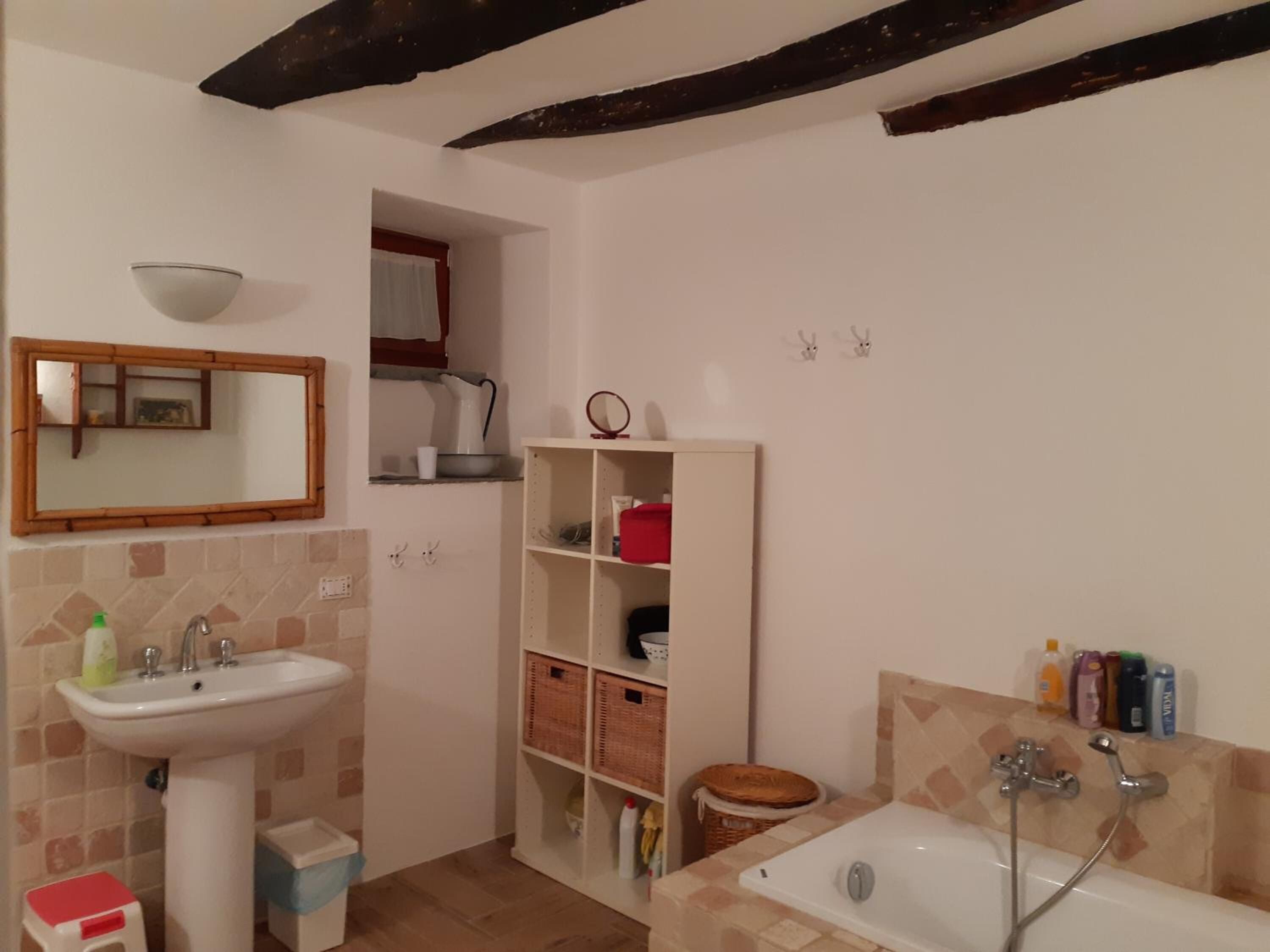 A bathroom with a sink, mirror, shelf, and bathtub.