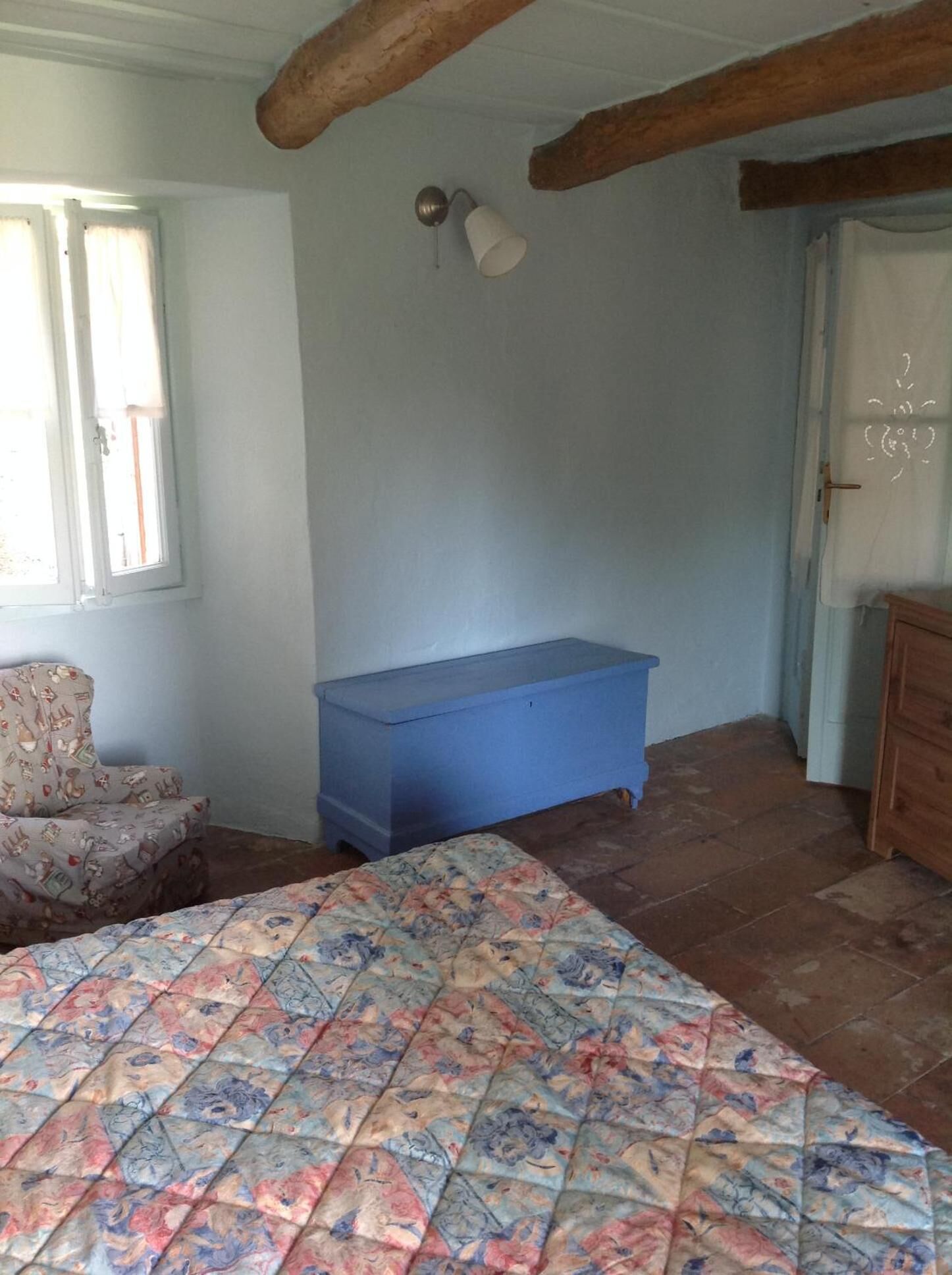 Ein Schlafzimmer mit einem Bett, einer blauen Kommode, einem Sessel und einem Fenster.