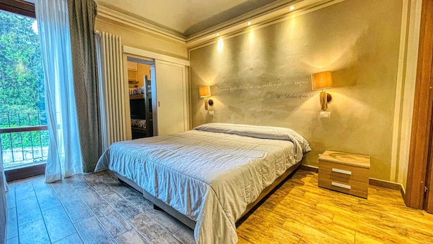 A bedroom with a bed, two wall-mounted lamps, a wooden nightstand, and a view of a balcony. - TABOR - APARTMENT sleeps 6 - 2nd floor (Bardonecchia)