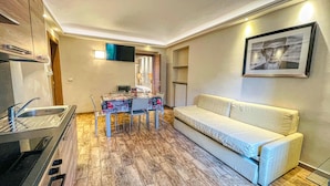 A compact living space with a kitchenette, a dining table, a sofa, and a flat-screen TV mounted on the wall. - TABOR - APARTMENT sleeps 6 - 2nd floor (Bardonecchia)