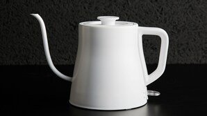 En vit tekanna med handtag och pip, placerad på en svart yta.