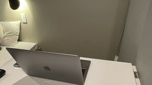 En bärbar dator står på ett vitt skrivbord, och på väggen sitter en lampa. Bredvid datorn finns en vit kudde.