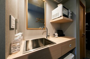 Un baño moderno con un lavamanos de acero inoxidable, un espejo, dispensador de toallas y un microondas sobre una estantería.