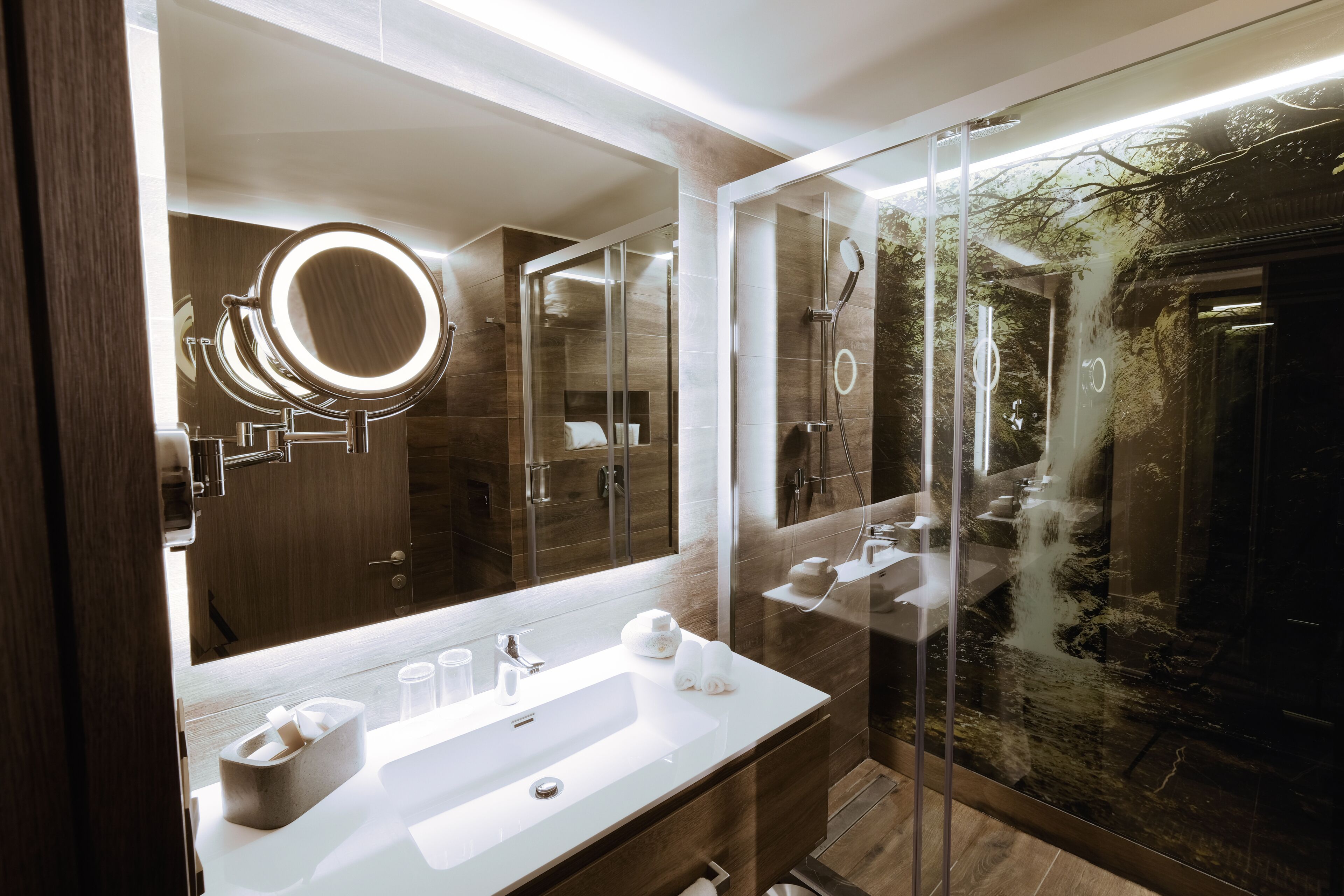 Un baño moderno con un espejo grande, un lavamanos y una zona de ducha con mampara de vidrio.