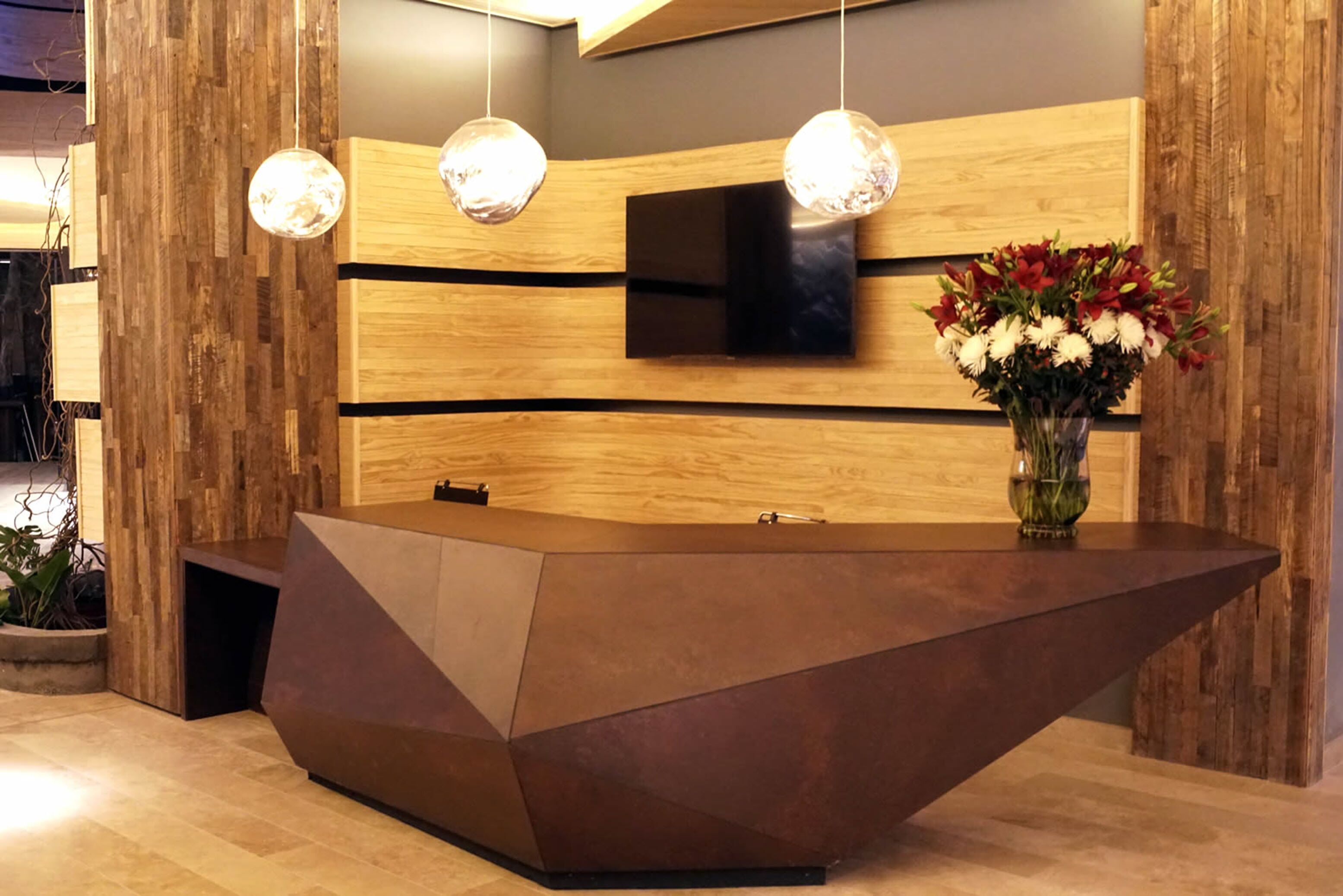 A reception desk with a modern design, a flat-screen TV mounted on the wall, and a vase of flowers.
