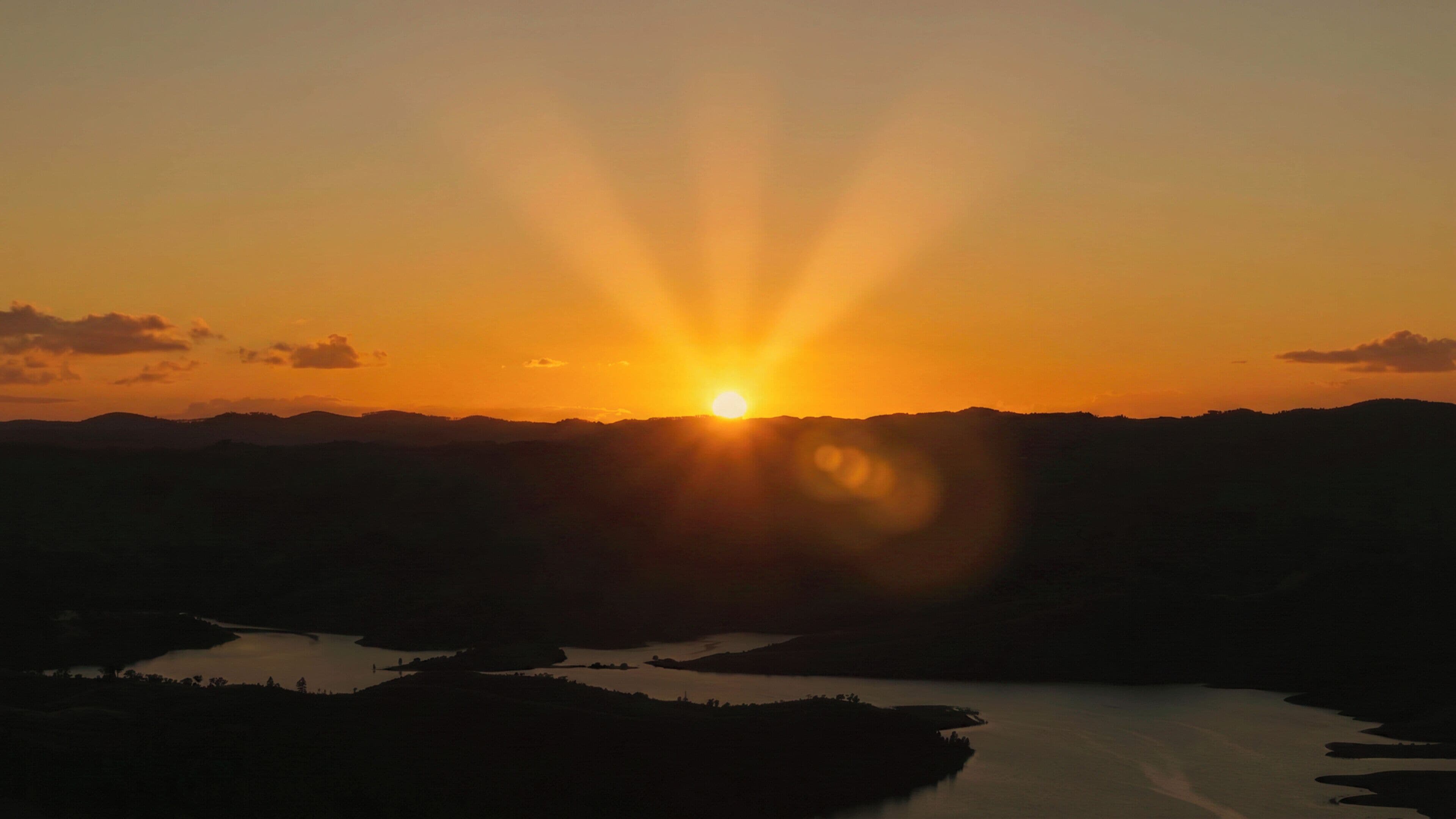 Un coucher de soleil sur un paysage montagneux, avec une étendue d'eau au premier plan.