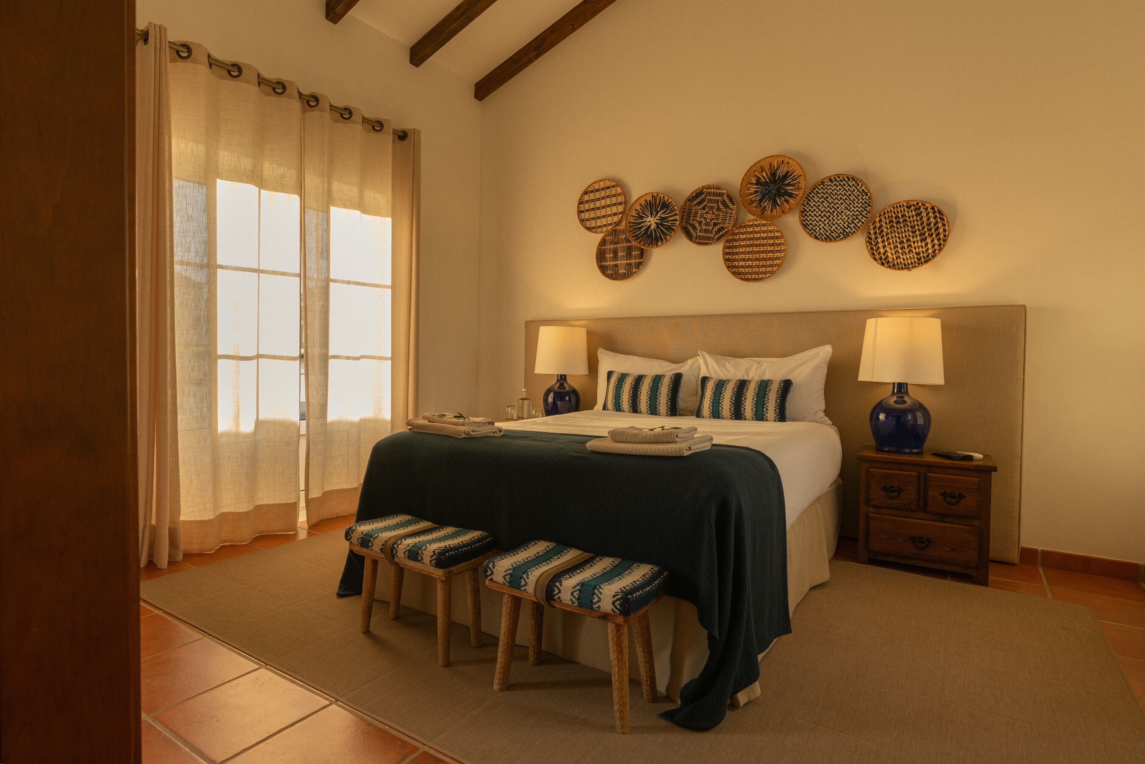 A bedroom with a bed, two bedside tables, a bench, and a wall with decorative plates.