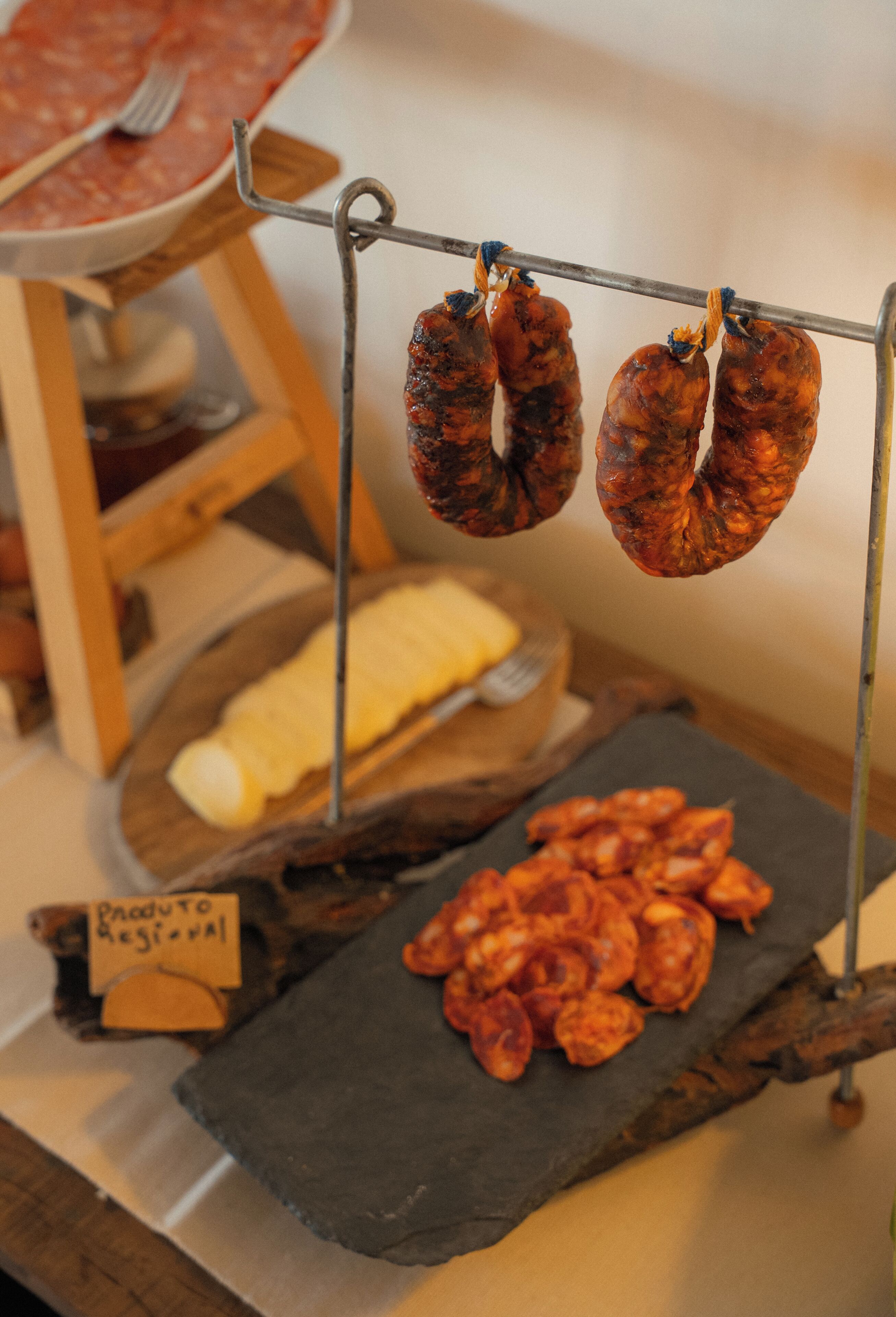 Exhibición de alimentos con salchichas colgantes, una tabla de quesos y un cartel que indica 'Producto Regional'.