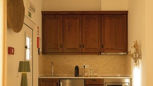 A compact kitchen with wooden cabinets, a stainless steel refrigerator, a microwave, and a small dining area with stools.