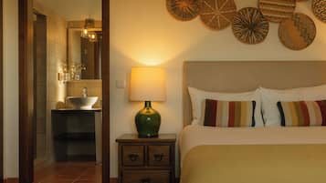 Habitación de hotel con cama, mesita de noche con lámpara, baño con lavamanos y espejo, y decoración en la pared.