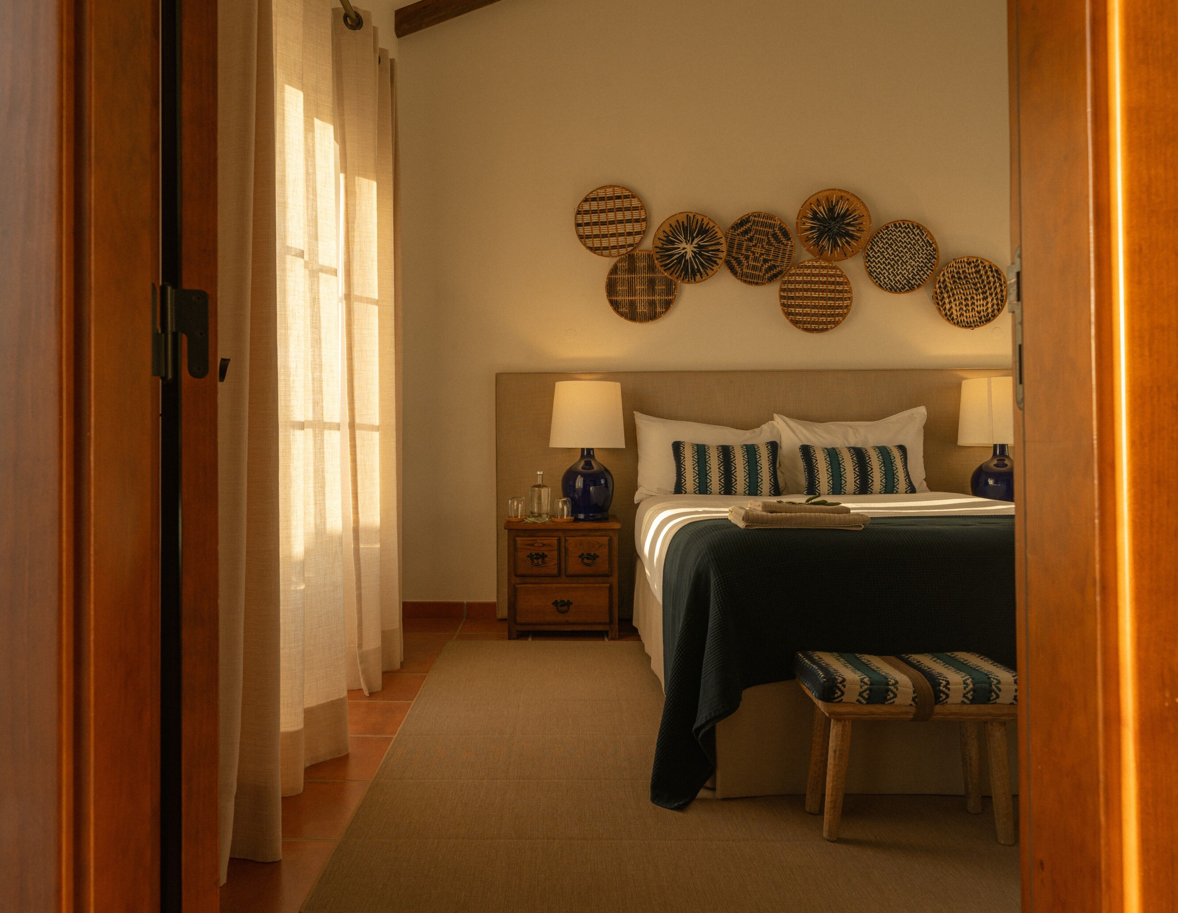 Un dormitorio con cama, mesitas de noche, un banco y adornos en la pared.