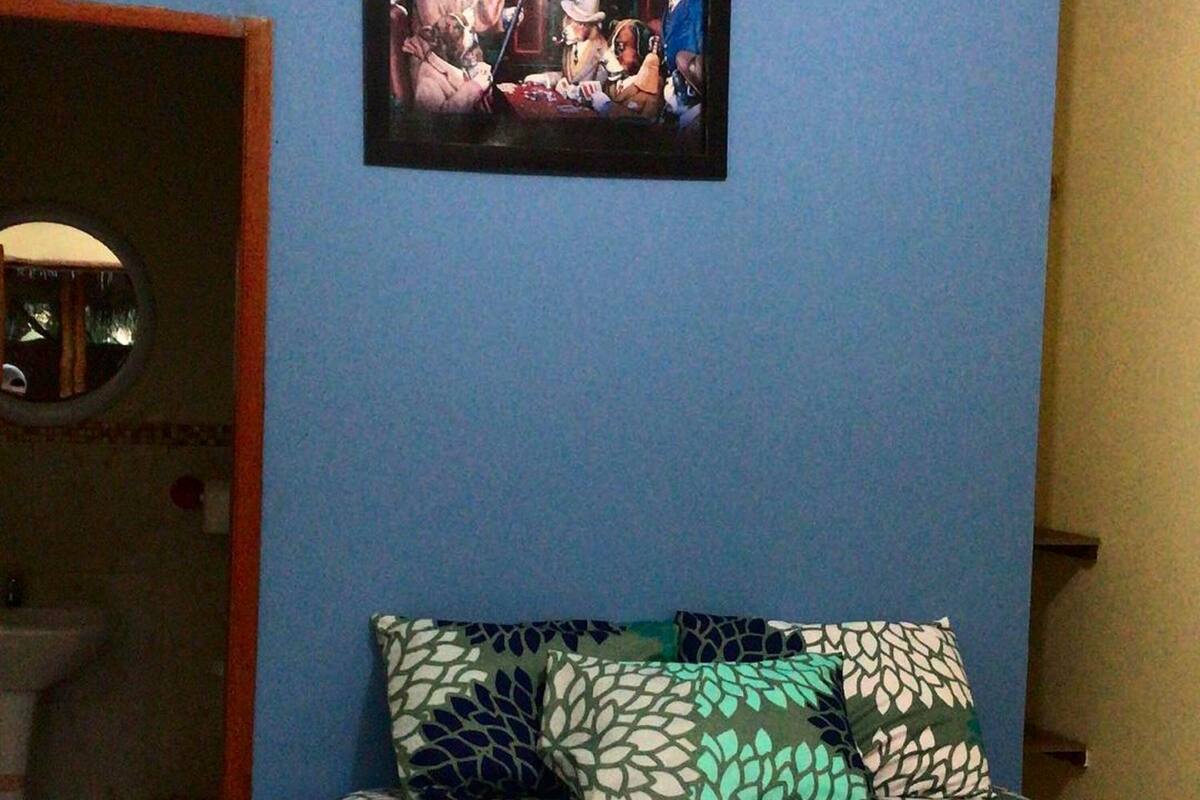 A bedroom with a bed, pillows, a framed picture on the wall, and a bathroom with a sink and mirror.