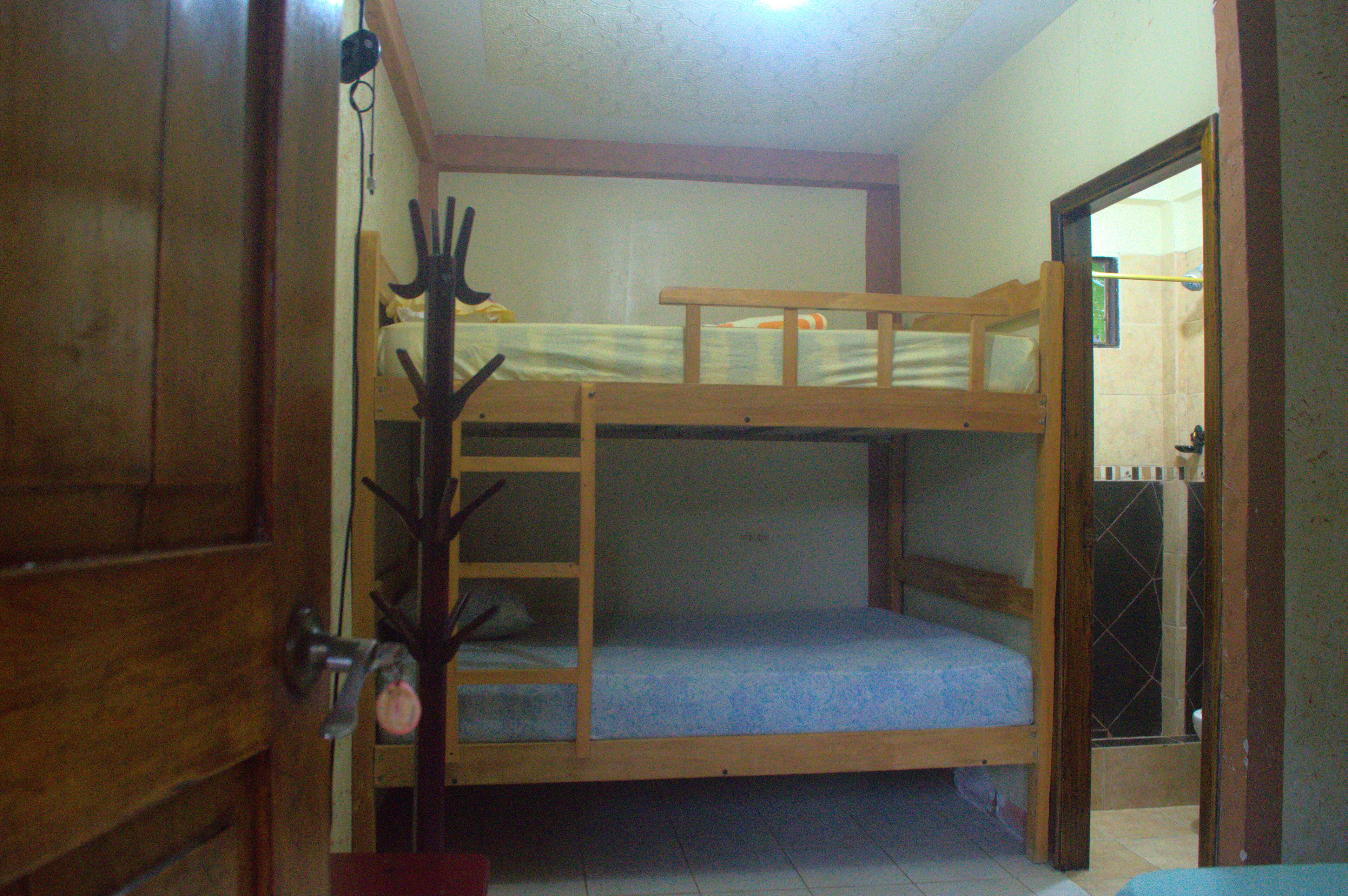 Une chambre avec un lit superposé, une porte en bois, une petite table et un porte-manteau.