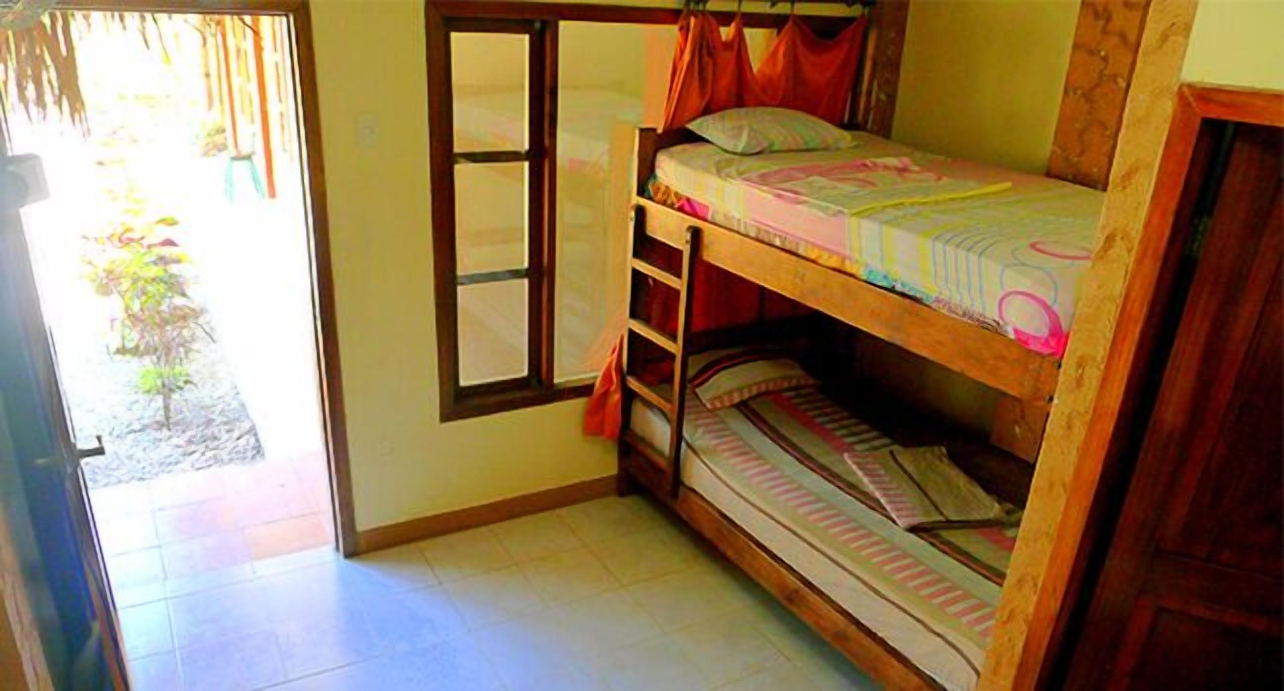 A dormitory room with a bunk bed, a window with curtains, and a door leading to an outdoor area.