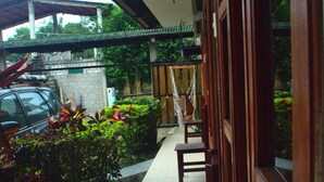 A covered outdoor area with a tiled floor, wooden benches, a hammock, and a car parked nearby. - Hostal Tierra y Mar (Manglaralto)