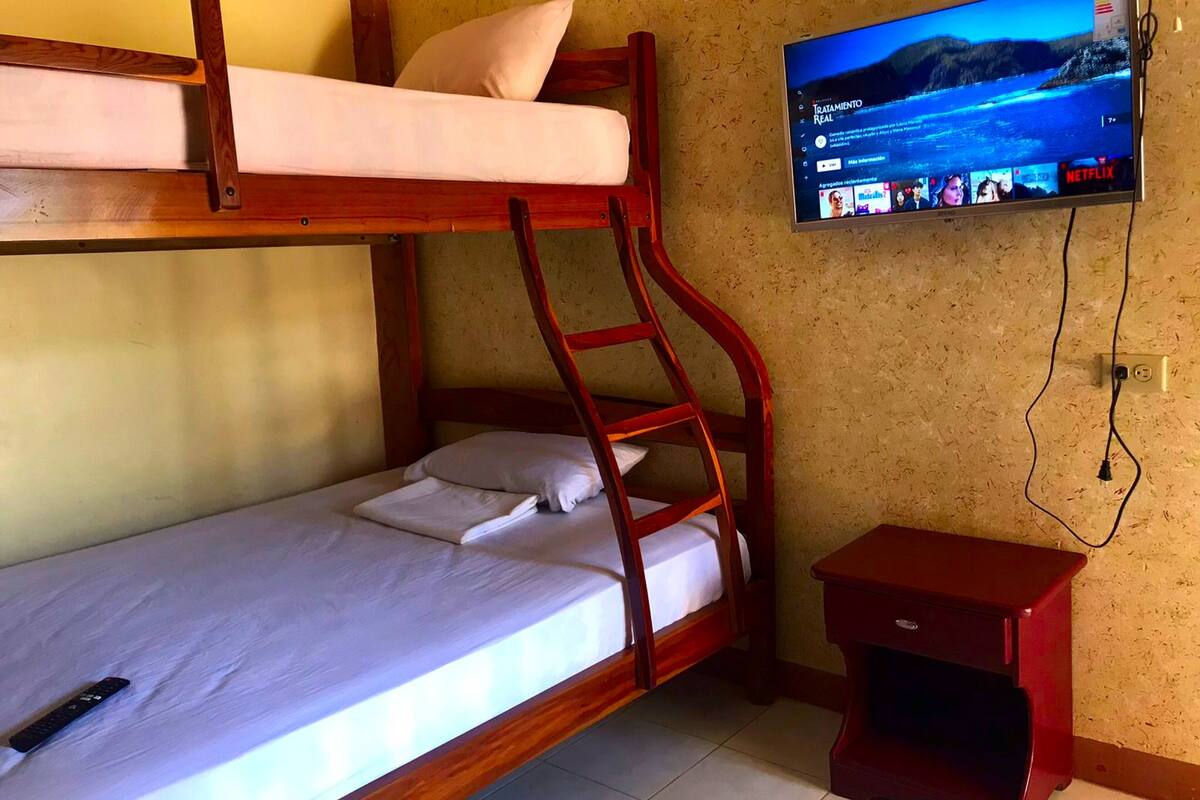 A bunk bed with a television mounted on the wall, a remote control on the bed, and a small red nightstand.