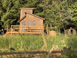 A rustic wooden cabin with a wooden deck and a barrel, surrounded by dense greenery. - Clydesdale Outpost (Amboy)