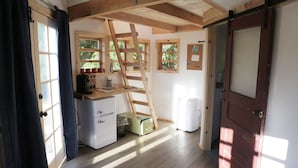 A compact room with a wooden desk, a ladder, a small refrigerator, and a door with a bulletin board. - Clydesdale Outpost (Amboy)