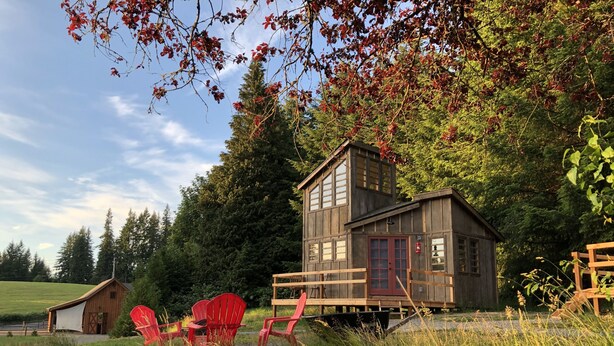 A rustic cabin with a wooden exterior, a red door, and a small porch with red chairs. - Clydesdale Outpost (Amboy)