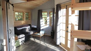 A cozy cabin with a wooden interior, a sofa, a small table, and a window with curtains. - Clydesdale Outpost (Amboy)