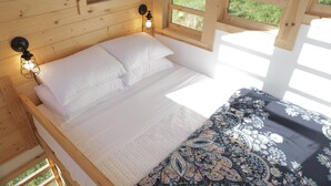A wooden cabin bedroom with a bed, two wall-mounted lights, and large windows. - Clydesdale Outpost (Amboy)