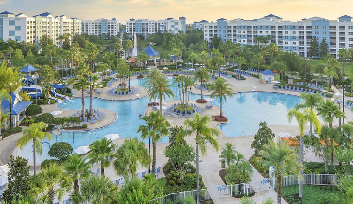 A resort with multiple swimming pools, palm trees, and a large building complex in the background.