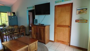 A room with a wooden dining table, chairs, a TV, and a door marked '1055 N 8569 W'. - Kolpin's Cabana cozy condo with 2 balconies to enjoy the tropical weather.  (Playa Del Coco)