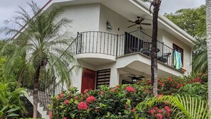 A two-story house with a balcony, surrounded by lush greenery and flowering plants. - Kolpin's Cabana cozy condo with 2 balconies to enjoy the tropical weather.  (Playa Del Coco)