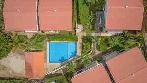 An aerial view of a residential area with multiple red-roofed houses, a central swimming pool, and surrounding greenery. - Kolpin's Cabana cozy condo with 2 balconies to enjoy the tropical weather.  (Playa Del Coco)