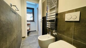 A modern bathroom with a bidet, a towel rack, and a shower area.