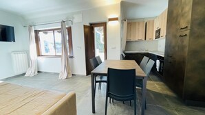 A modern kitchen with wooden cabinets, a dining table with chairs, and a large window with curtains.