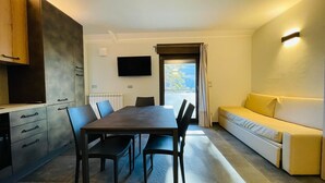 A modern living room with a dining table, chairs, a sofa, and a TV mounted on the wall.