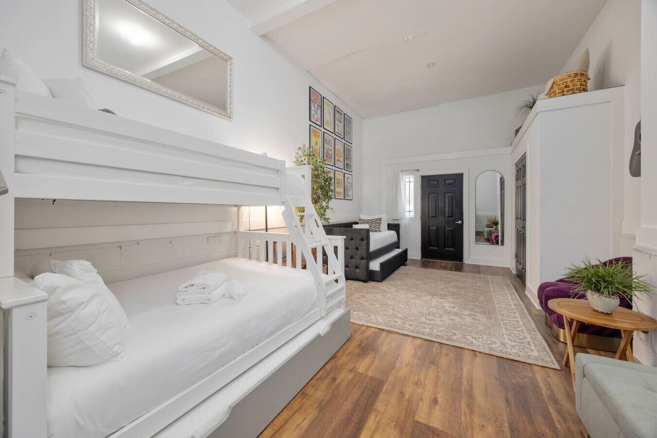 A bedroom with a bunk bed, a bedside table, a chair, a small table with a plant, and a door leading to another room.