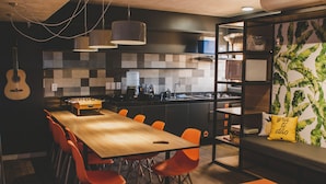A modern kitchen with a large island, a dining area with orange chairs, and a cozy seating area with a sofa and cushions. - Wanderlust Hostel (Maceió)