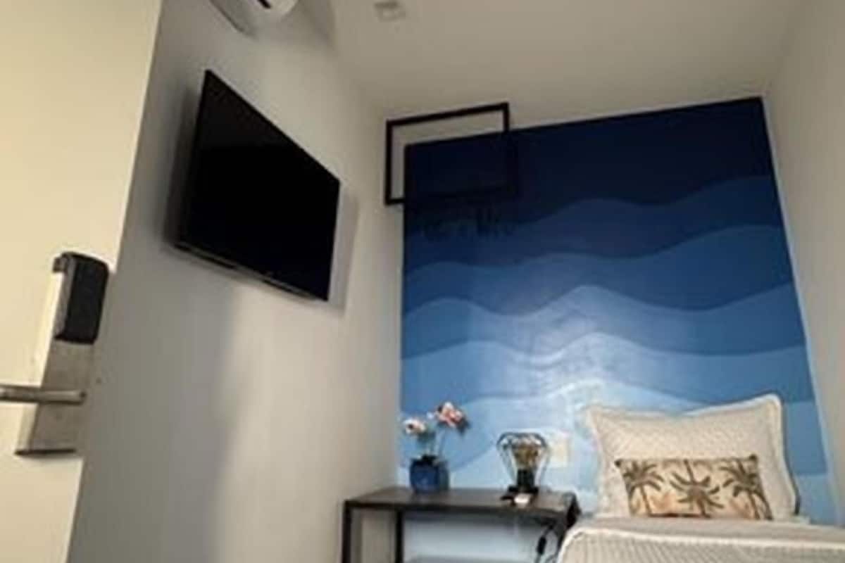 Quarto de hotel com cama, escrivaninha com computador, televisão de tela plana e ar-condicionado.