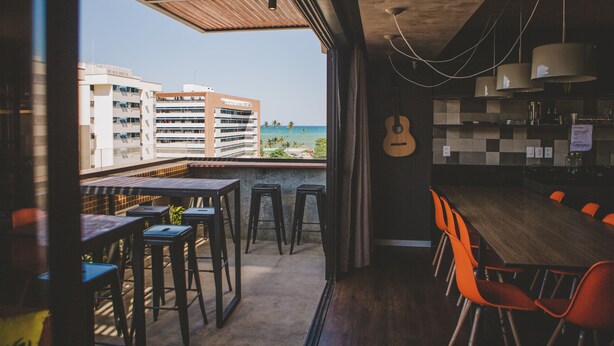 A modern bar area with a view of the beach and buildings. - Wanderlust Hostel (Maceió)